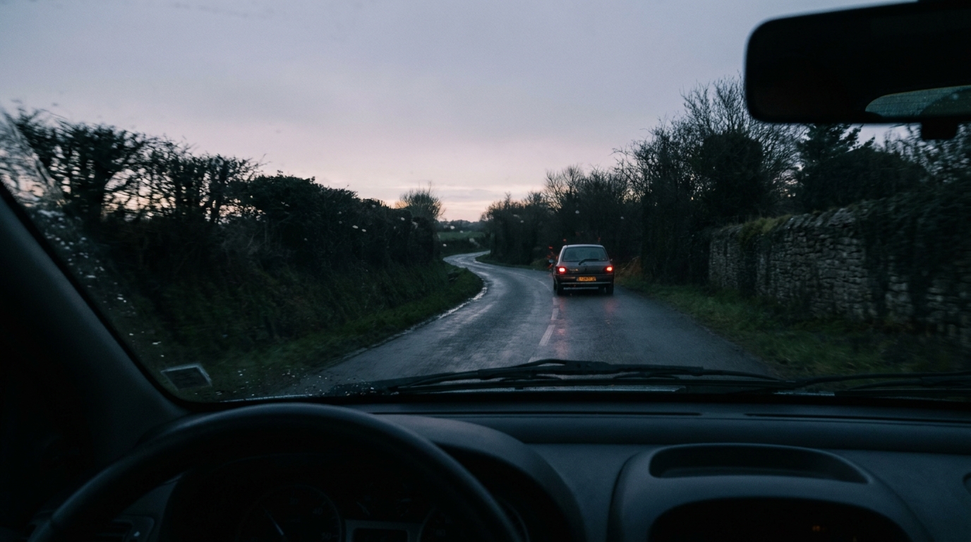 Une route de campagne en Bretagne au crépuscule, vue depuis l'intérieur d'une voiture, avec une Clio grise au loin.